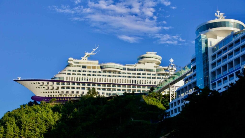 The Sun Cruise Resort & Yacht, a hotel uniquely shaped like a ship, majestically perched on a cliff overlooking the East Sea near Jeongdongjin, under a clear blue sky.
