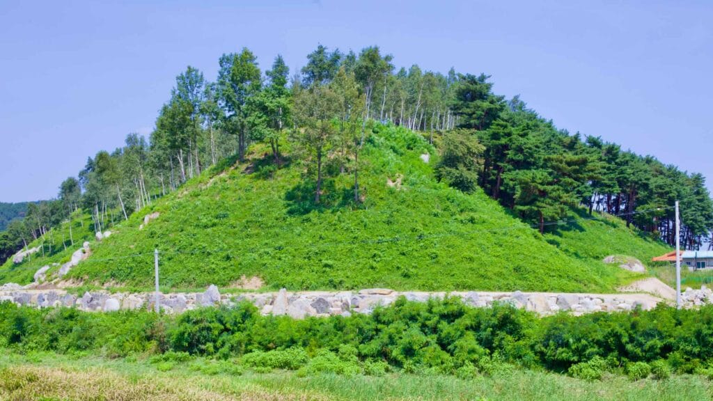 Near the Bukcheon Railroad Bridge, a unique hill rises, with one side covered in lush green grass and the other adorned with dense trees.