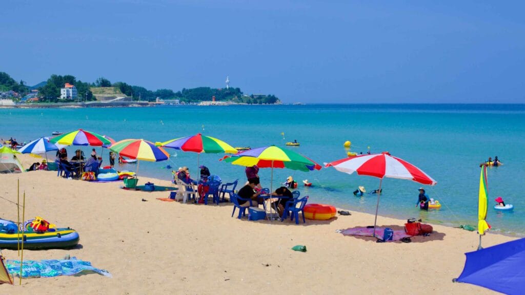 Vibrant rainbow-colored parasols dot Chodo Beach along the East Sea's blue waters.