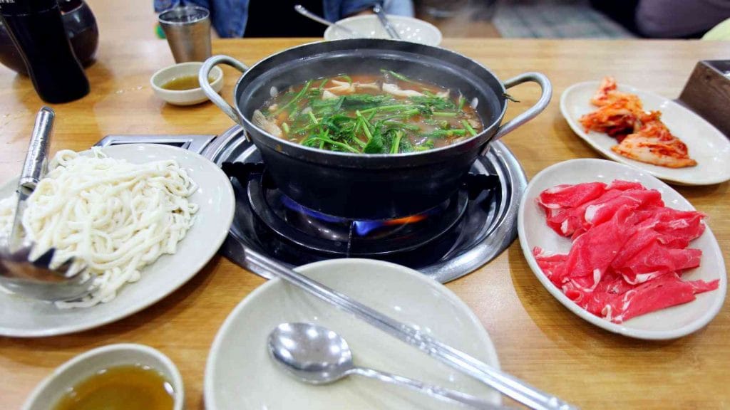 A picture of noodles cooking in a pot in a restaurant in Korea.