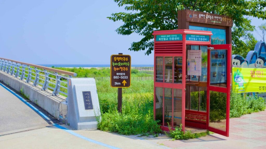 Bukcheon Railroad Bridge Certification Center, a red booth for cyclists to stamp their bike passports, overlooks green marshland leading to the East Sea.