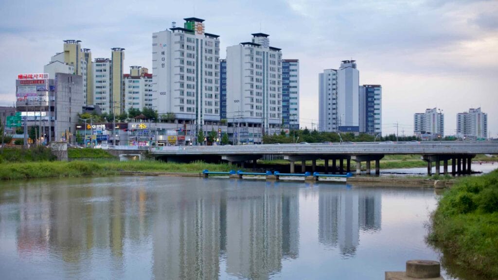 High-rise apartments and commercial buildings reflect on the calm waters of Bogang Stream in Jeungpyeong.
