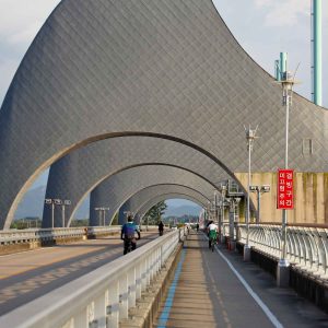 A path runs beneath the towering rice grain-shaped arches of Seungchon Weir.