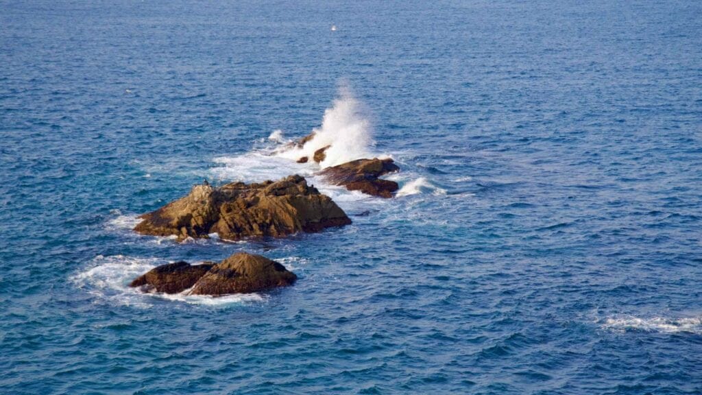 Waves crash against the rocks in the East Sea, creating white sea spray over the blue waters near the Chogok Yonggul Cave Hiking Trail.