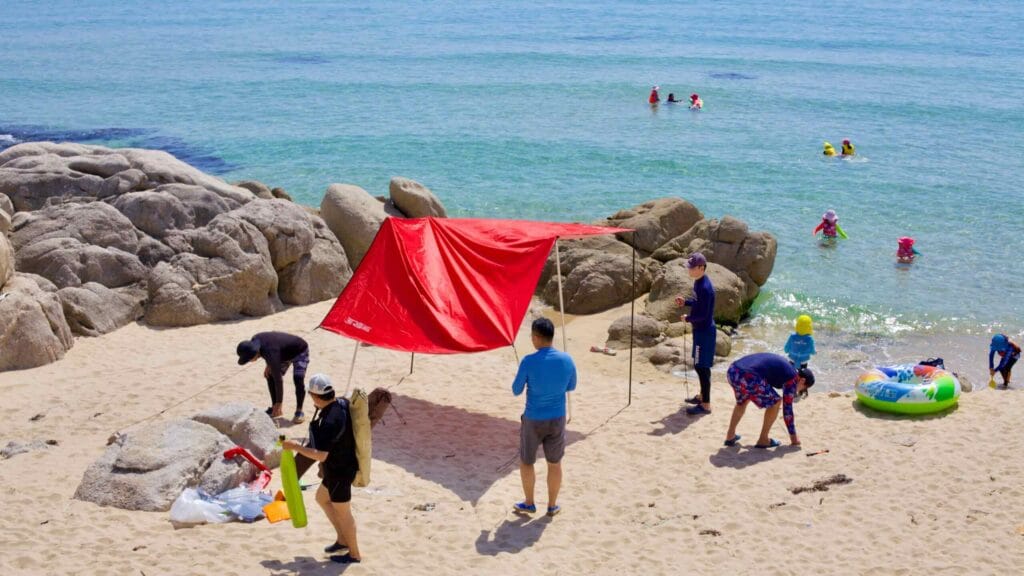 On the sandy shores of Gonghyeonjin Beach, a family sets up a pop-up tent near striking rock formations.