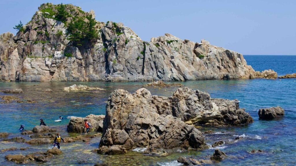 Adventurers explore the shallow, rocky waters between the coast and a towering rock formation in the East Sea near Geojin Port.
