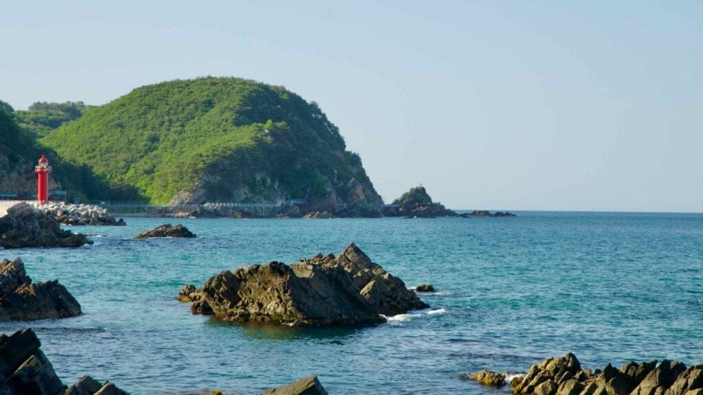 The rocky coastline of Simgok Port and Heonhwa Road with its distinctive red lighthouse.