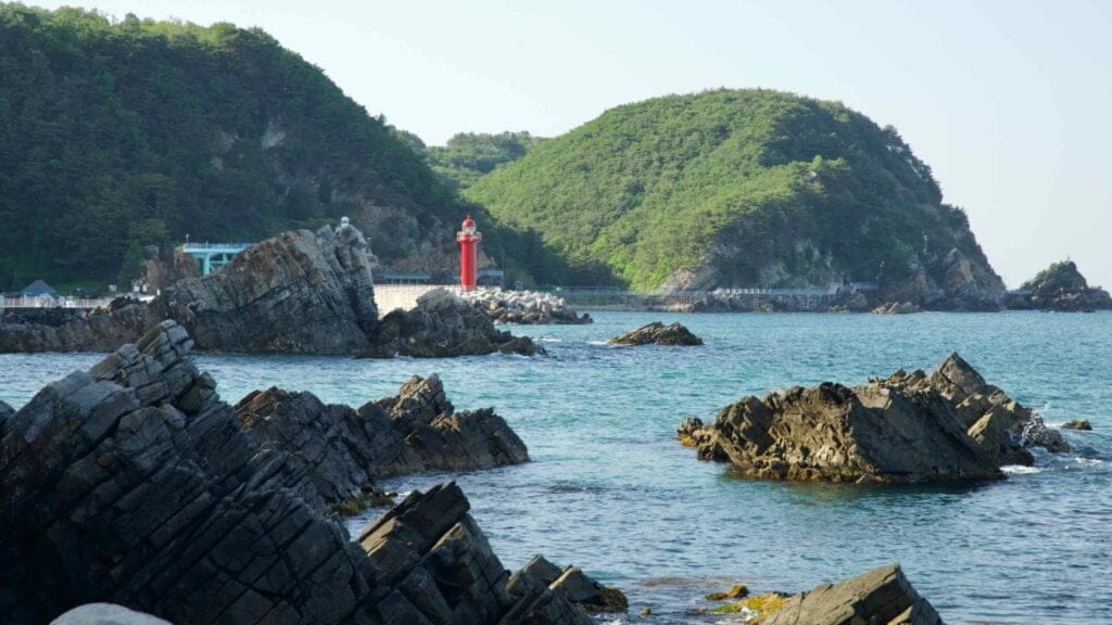 Simgok Port's red lighthouse stands out against the green hills and rocky coastline.