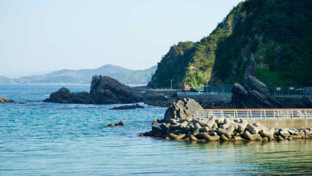 Heonhwa Road winds along the rocky coastline of the East Sea. The rugged cliffs and concrete wave breakers provide a dramatic contrast.