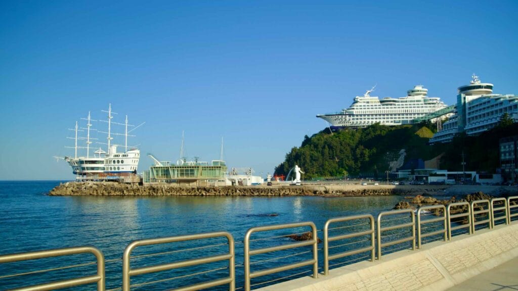 A view of Jeongdongjin Port featuring the distinctive tall ship restaurant Fish Soup and the iconic Sun Cruise Resort perched on the hillside.