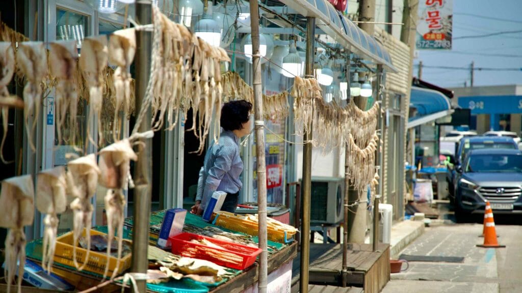 A vendor standing beside rows of dried squid hanging outside a shop at Samcheok Port.