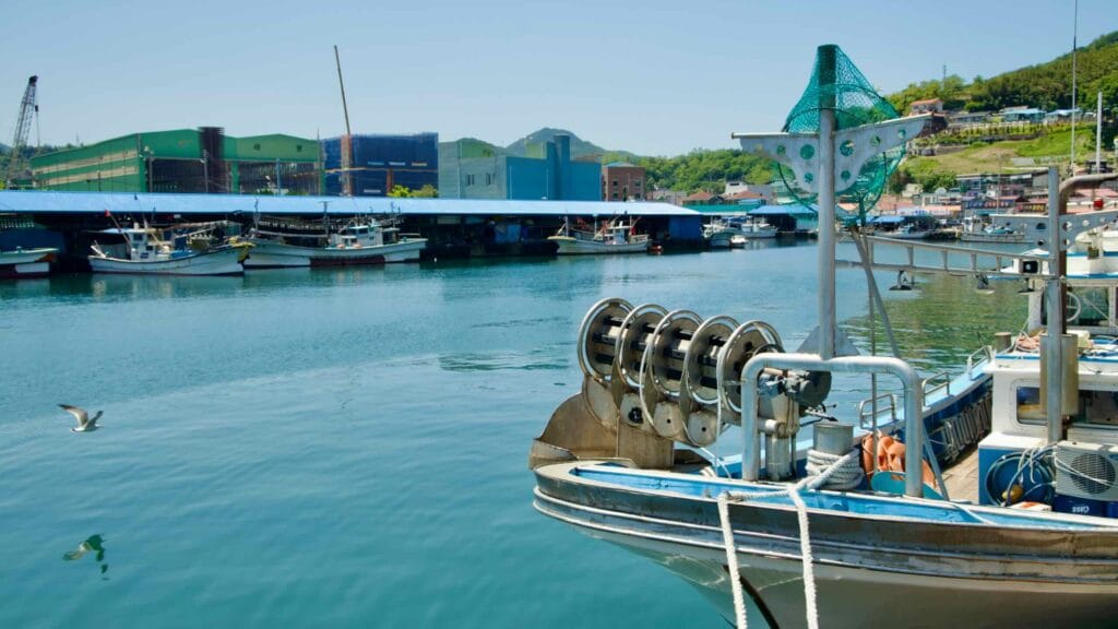 Fishing boats docked at Samcheok Port with industrial buildings in the background.