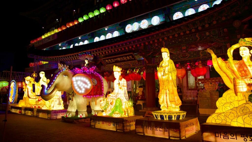 Glowing Buddhist figures stand outside the entrance of Jeonggwangsa Temple at night.