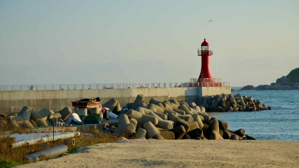The red lighthouse at Bongpo Port stands near a collection of tetrapods along the shore.