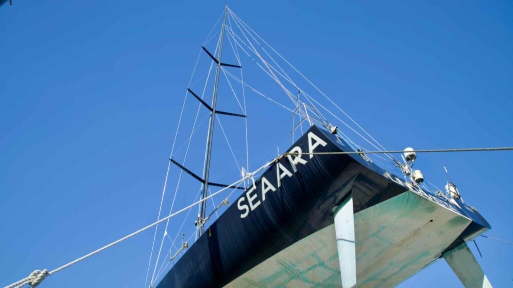 A detailed view of the sailboat "Seaara" in dry dock at Susan Port Marina, showcasing its hull and mast under a vibrant blue sky.