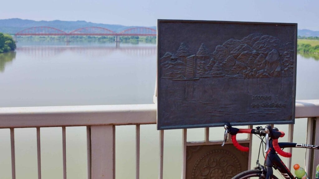 A road bike rests on the railing of Baekje Bridge, next to a historical plaque of the Geum River.