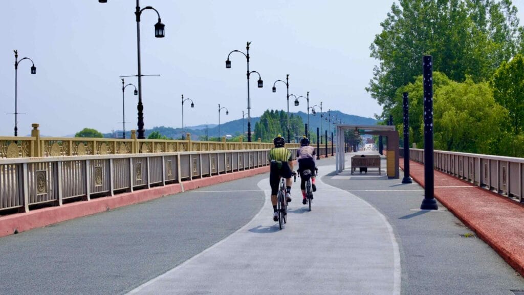 Two cyclists ride on the dedicated bike lane of Baekje Bridge, which offers scenic river views.