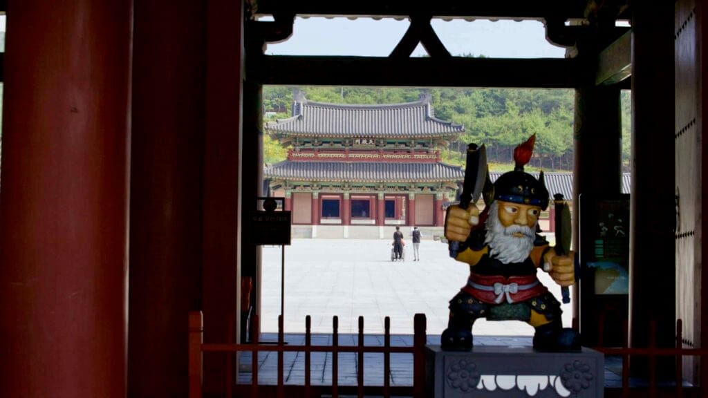 A guardian statue stands at the entrance of Baekje Cultural Land, overlooking the palace-style buildings.