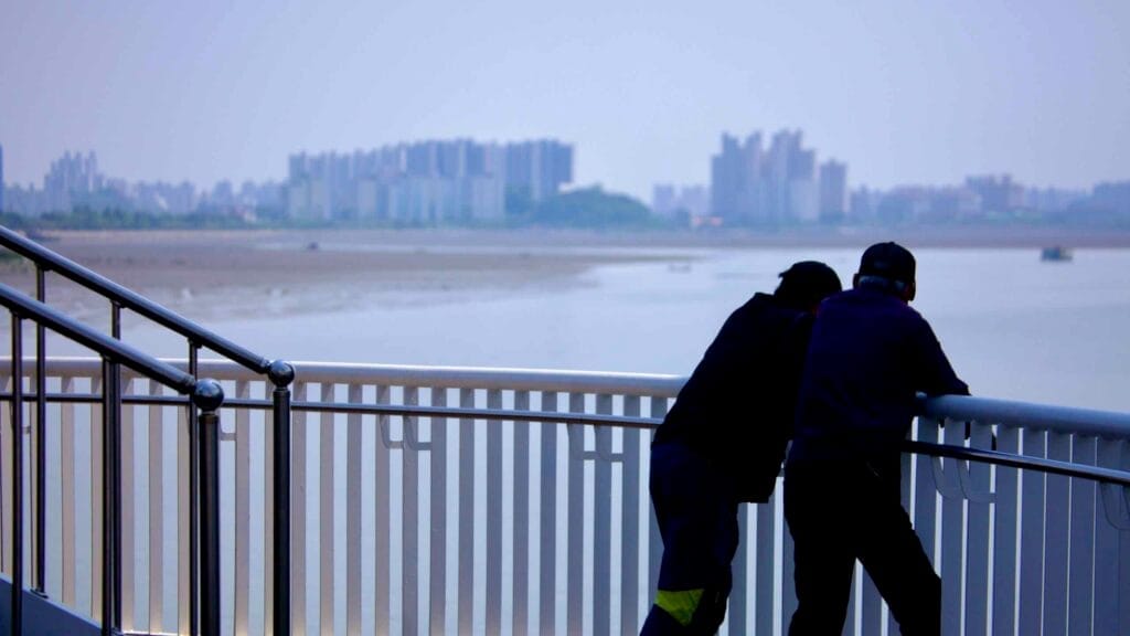 Men lean against a railing, gazing at the Geum River Estuary, where the river meets the Yellow Sea.