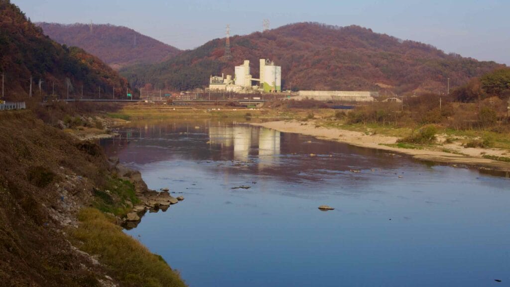 A factory complex stands at the foot of forested hills on the Geum River.