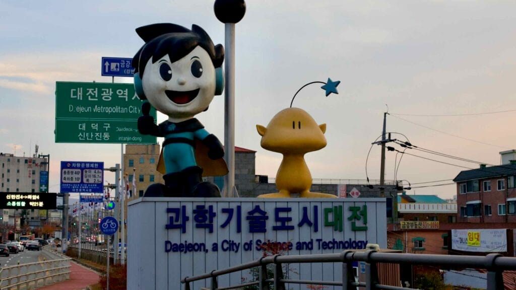 Large cartoon mascots stand atop a sign reading “Daejeon, a City of Science and Technology."