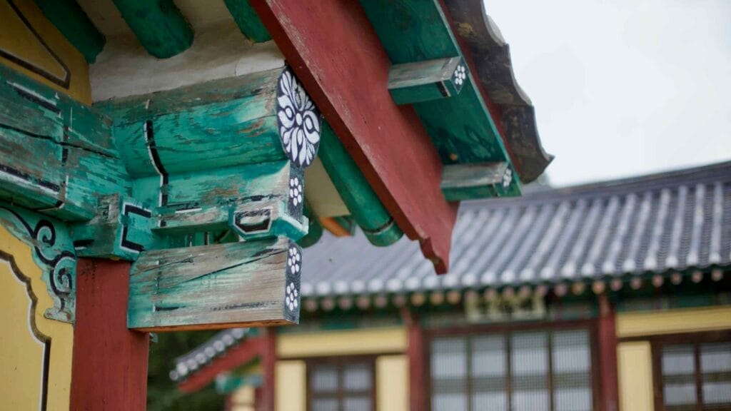 A close-up of the vibrant wooden eaves at Yeonpung Hyanggyo, showcasing traditional Korean architectural details and faded dancheong patterns on this historic Confucian school.