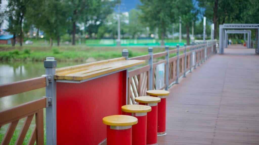 A seating area with red stools and a wooden table on a pedestrian bridge in Baekro Park.