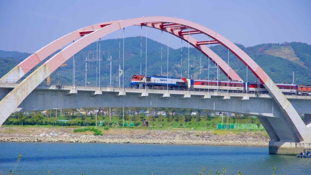 A KORAIL train passes over a modern arched railroad bridge spanning the Seomjin River.