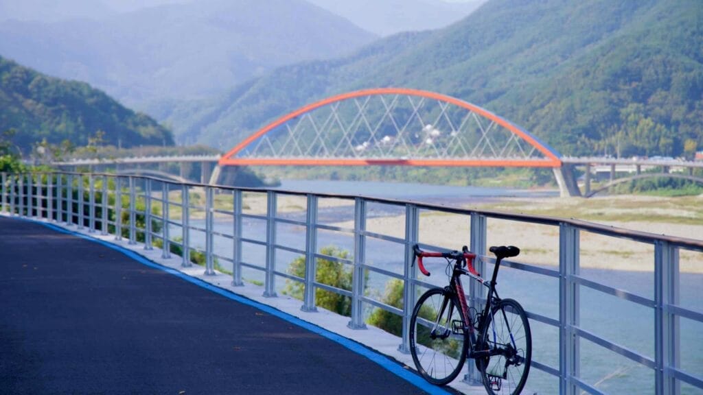 A bike along the railing of the Seomjingang Bike Path, with Namdo Bridge spanning the Seomjin River.