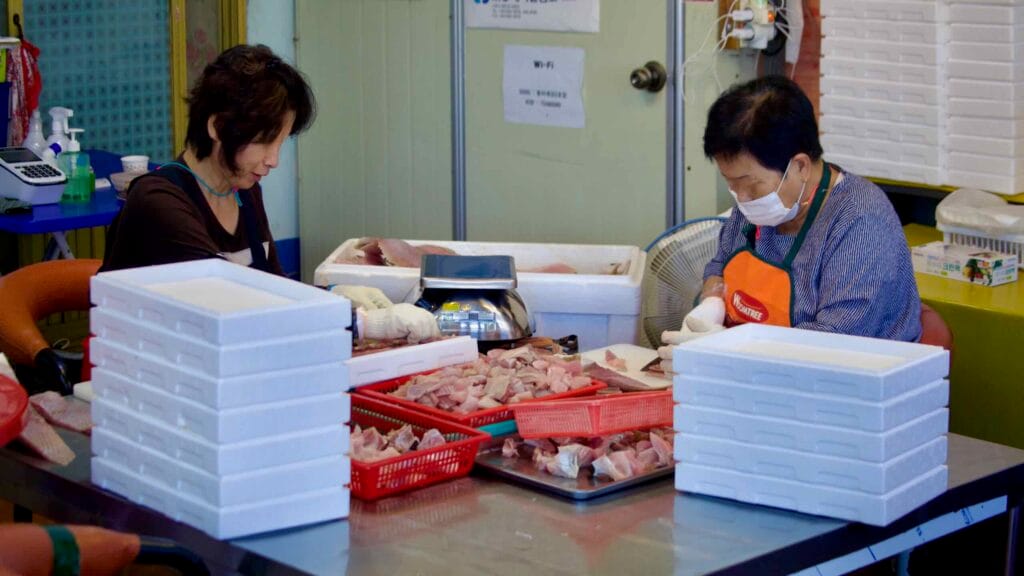 Two workers carefully prepare hongeo-hoe, the fermented skate dish famous in Naju, slicing and packing the pungent delicacy at a seafood shop on Hongeo Street.