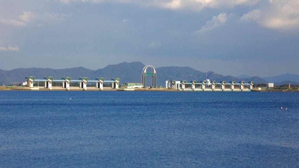 A view of the Yeongsan River Estuary Bank, a vital infrastructure project preventing saltwater intrusion and supporting regional agriculture. The Landmark Tower rises above the structure, symbolizing the transformation of the river.