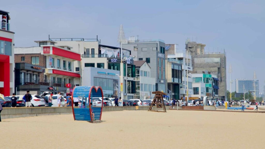 Colorful beachfront buildings face Anmok Beach, with a lifeguard tower.