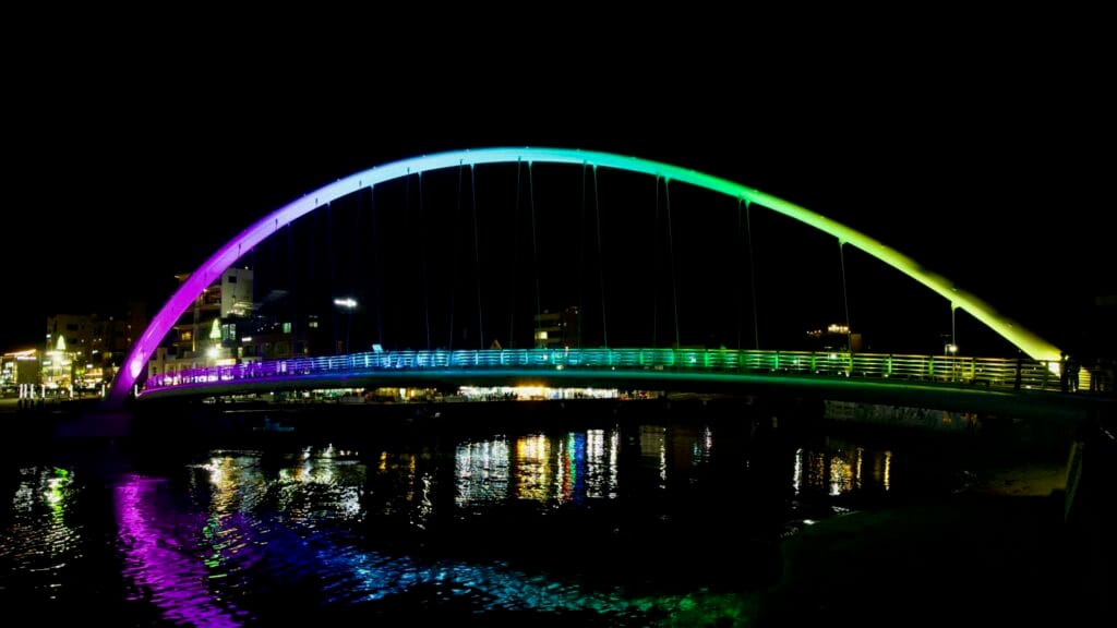 Gangmun Sotdae Bridge glows in shifting rainbow hues, casting colorful reflections across the harbor waters.