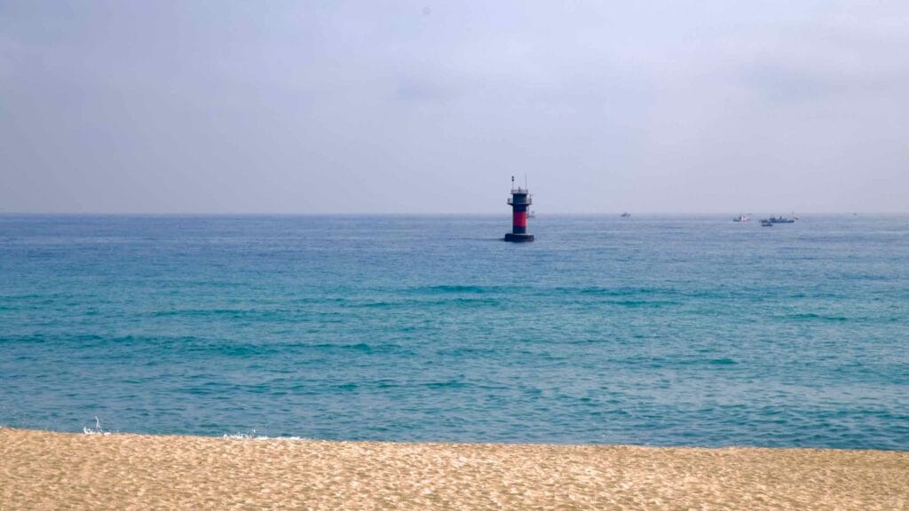 Solitary offshore navigation beacon beyond the quiet sands and emerald waters of Gyeongpodae Beach.