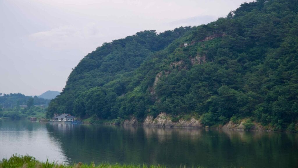 Forested cliffs of Buso Mountain rise above the Geum River, marking Nakwaam Rock.