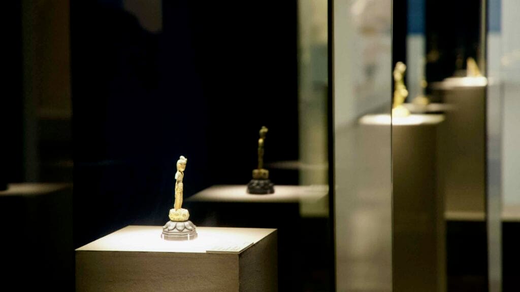 Row of small gilt bronze Buddha statues in glass cases at Buyeo National Museum.