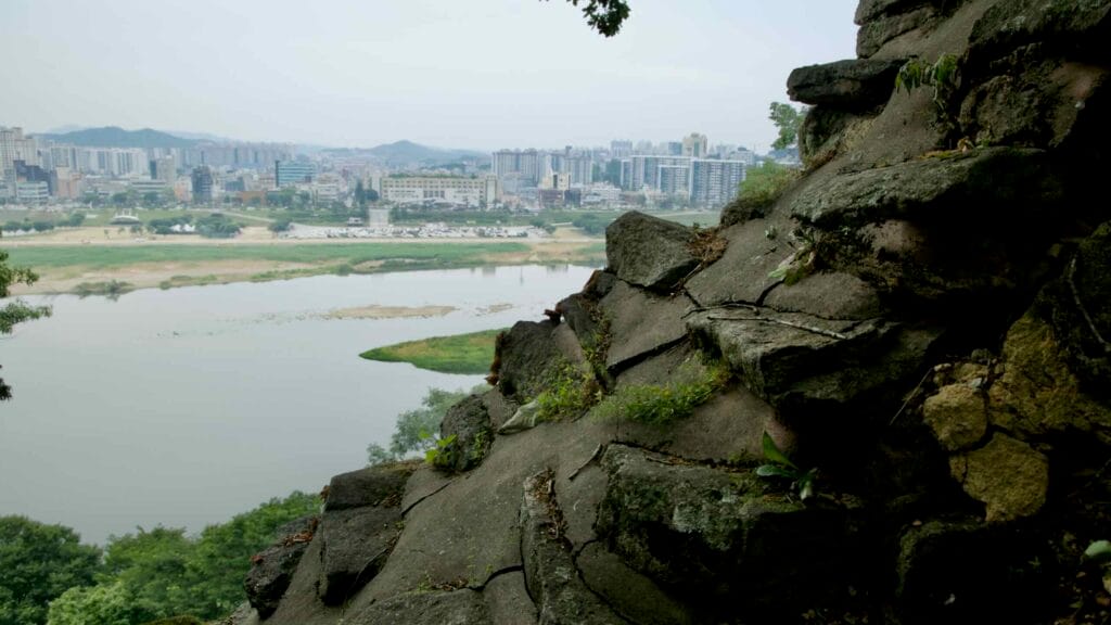 Collapsed stonework at Gong Mountain Fortress overlooks the Geum River and city skyline.