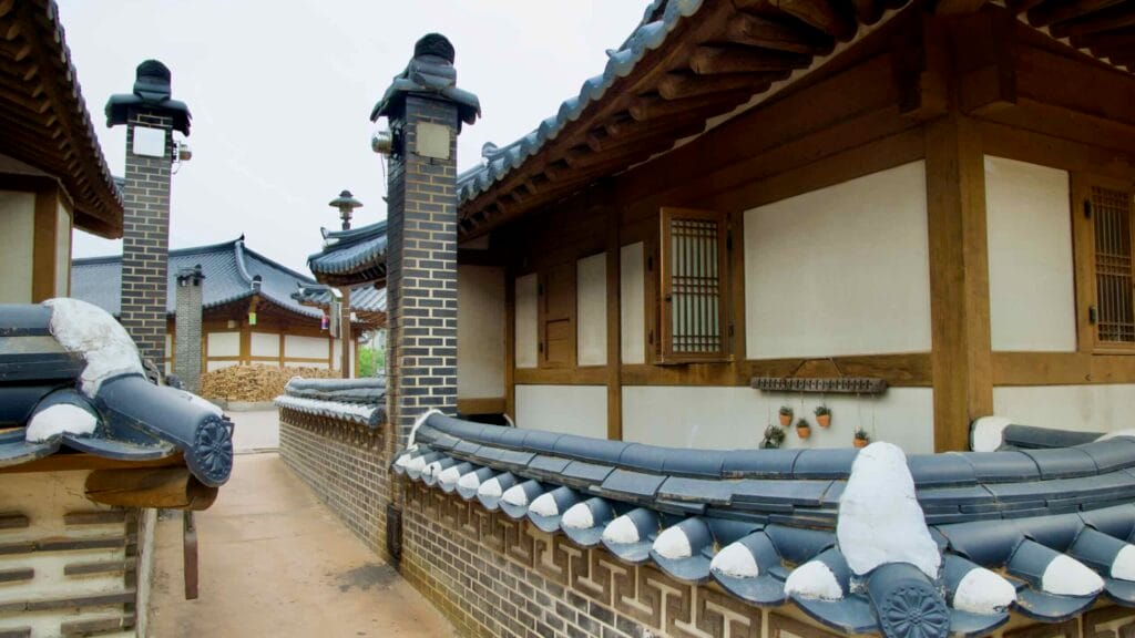 A narrow alley runs past tiled brick walls, open windows, and chimney stacks in a quiet corner of Gongju Hanok Village.