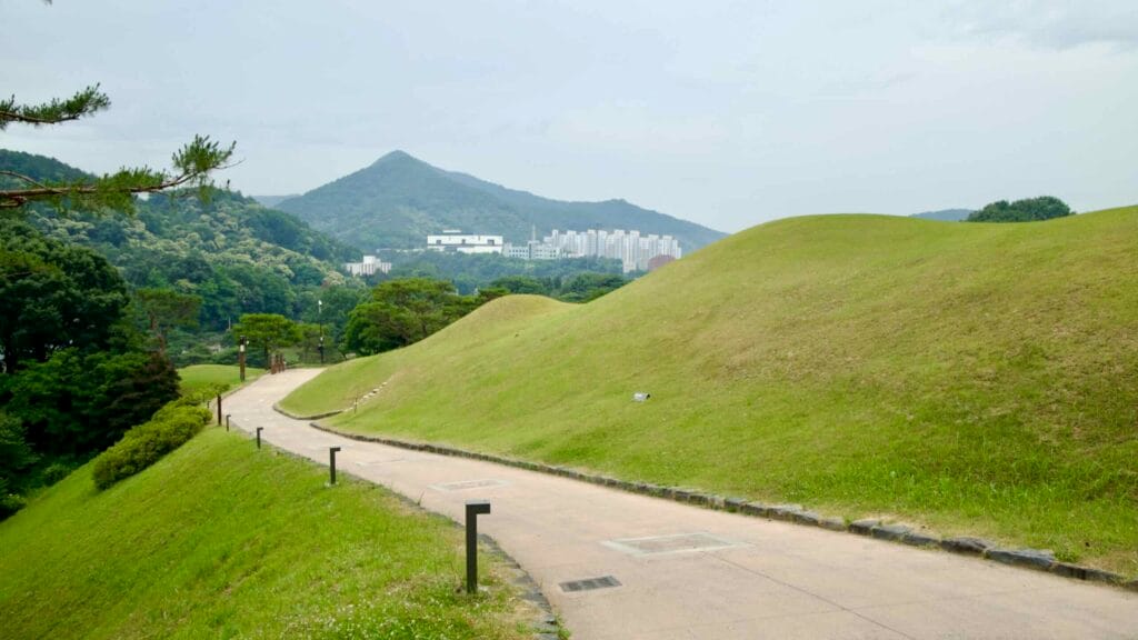 Winding path through Baekje burial mounds at Songsan-ri, with a distant view of Gongju's skyline.