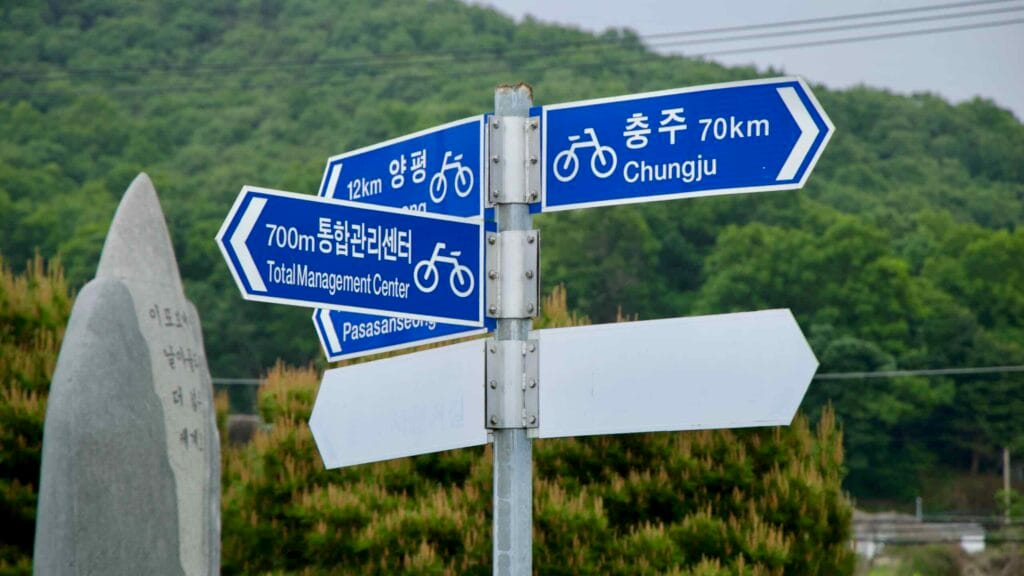 A directional cycling signpost near Ipo Weir points the way to nearby destinations like Yangpyeong and Chungju along the scenic South Han River bike route.