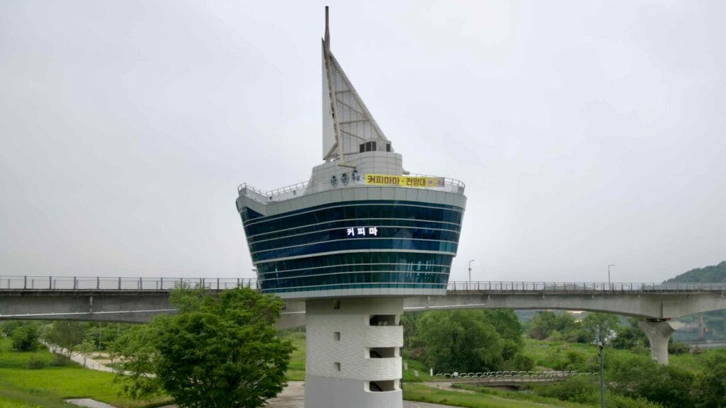 The Ipo Weir Observatory, designed like a sailboat, rises from the riverbank beside the bridge-top cycling and walking path along the South Han River.