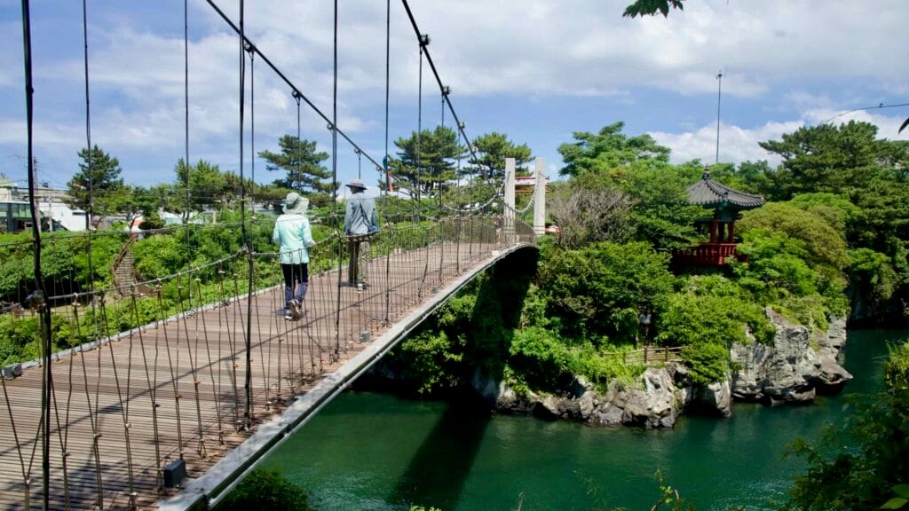 Walkers cross Yongyeon Cloud Bridge above emerald water at Yongdam Park.