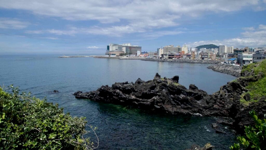 Jeju City skyline and harbor beyond lava rocks near Yongduam.