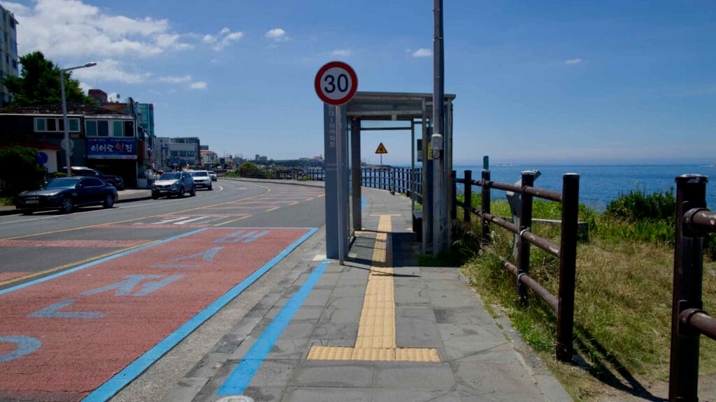 Seaside bus stop with blue bike lane along Jeju’s Hagu‑Aewol coast.