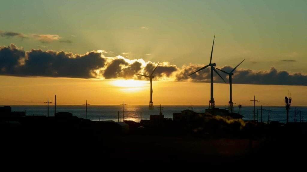 Sunset light breaks beneath cloud bands behind offshore wind turbines.