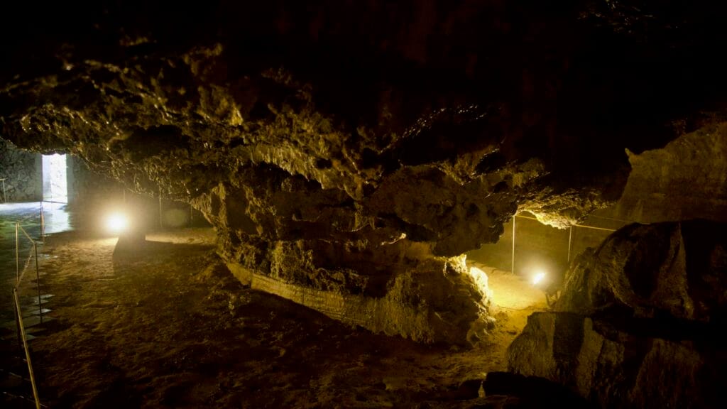 Layered rock overhang with lights and a side opening in Hallim Park’s lava cave.
