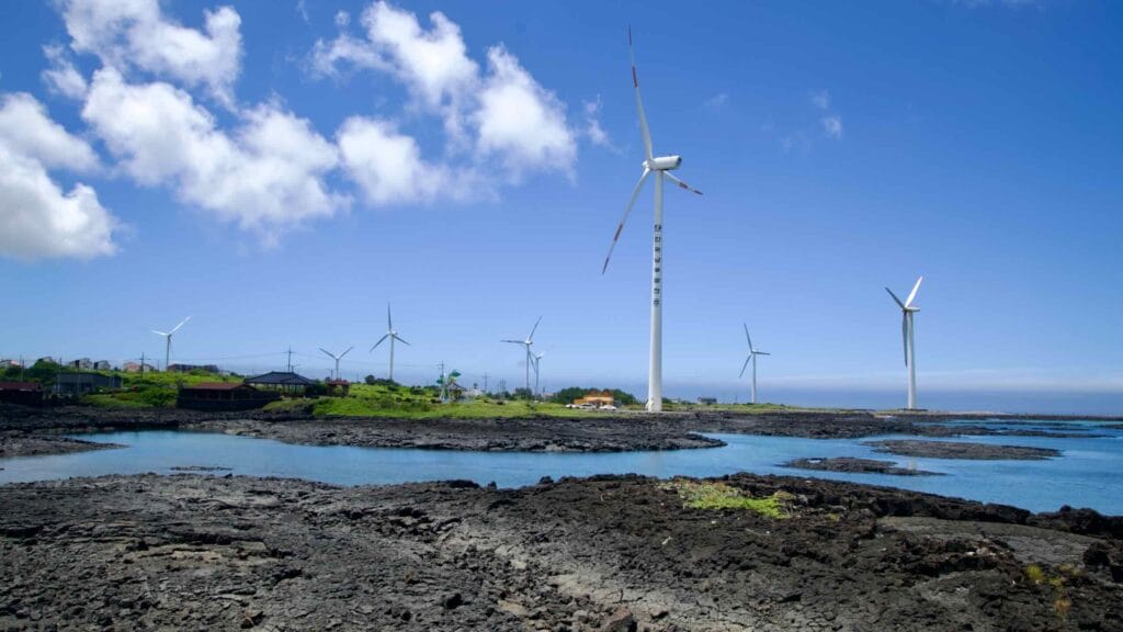Rows of wind turbines sweep over Jeju’s black‑lava shoreline at Sinchang.