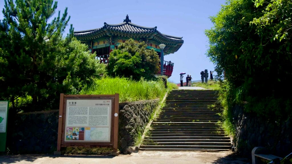 Suwolbong pavilion above steps and information boards with visitors.