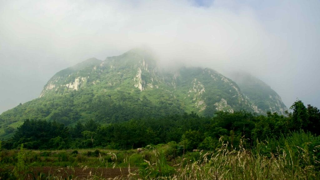 Fields and stone walls below cloud‑topped Sanbang Mountain.