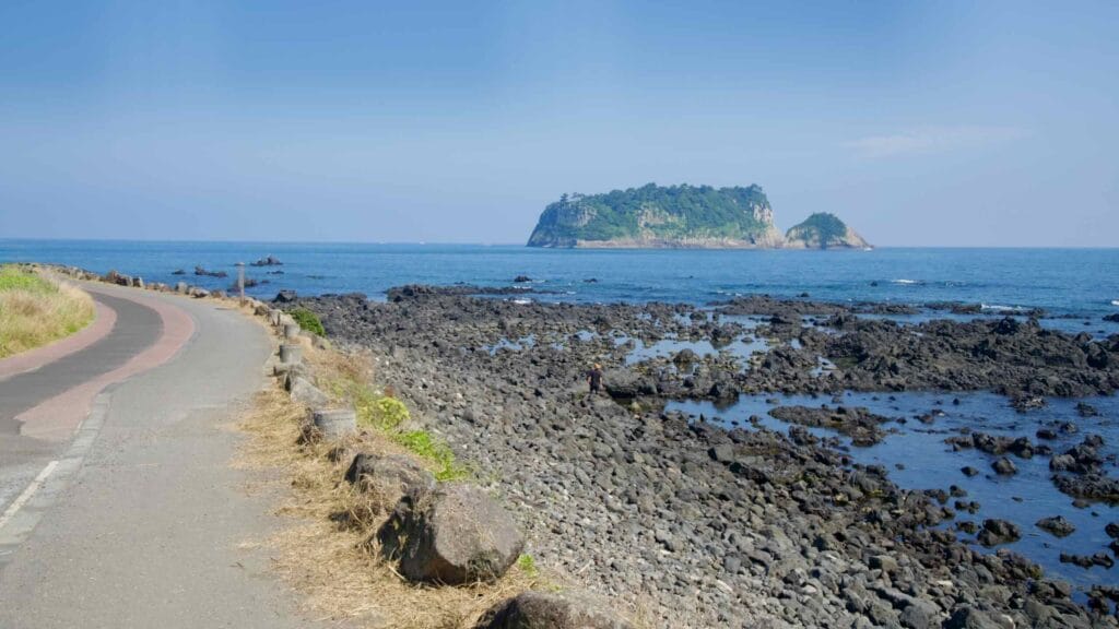 A seaside path curves beside the rocky shore with views toward Beomseom.